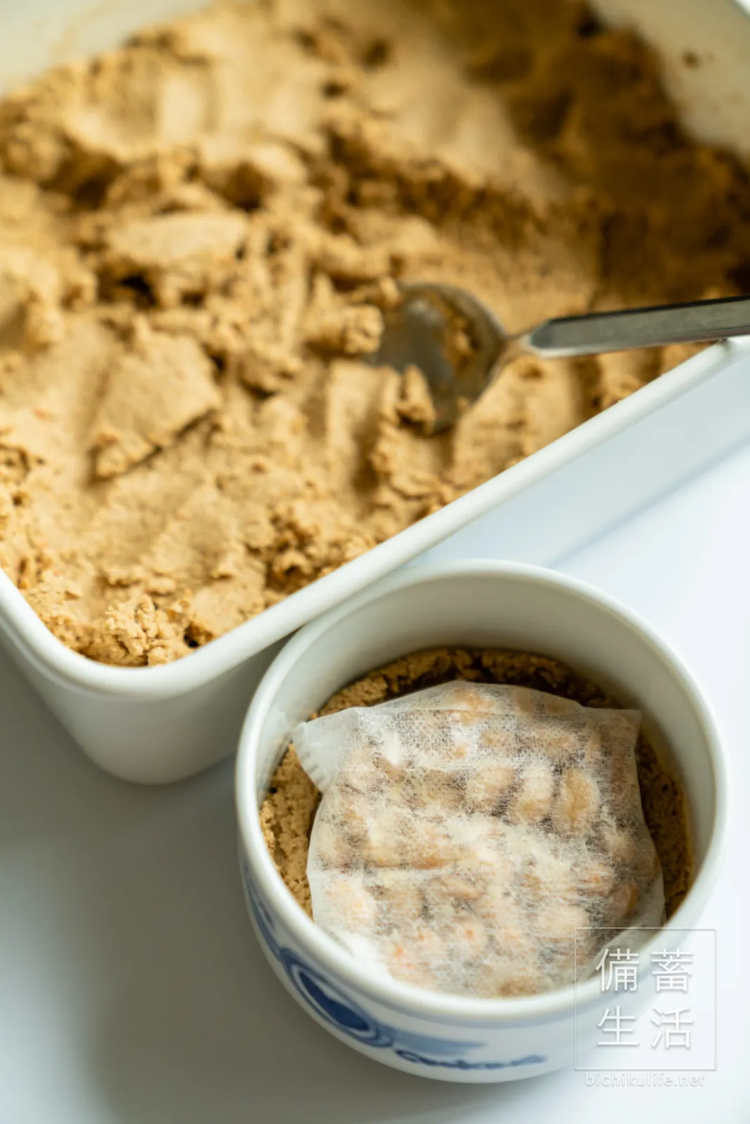 別の容器に取り分けたぬかに、お茶パックごと納豆を入れるところ
